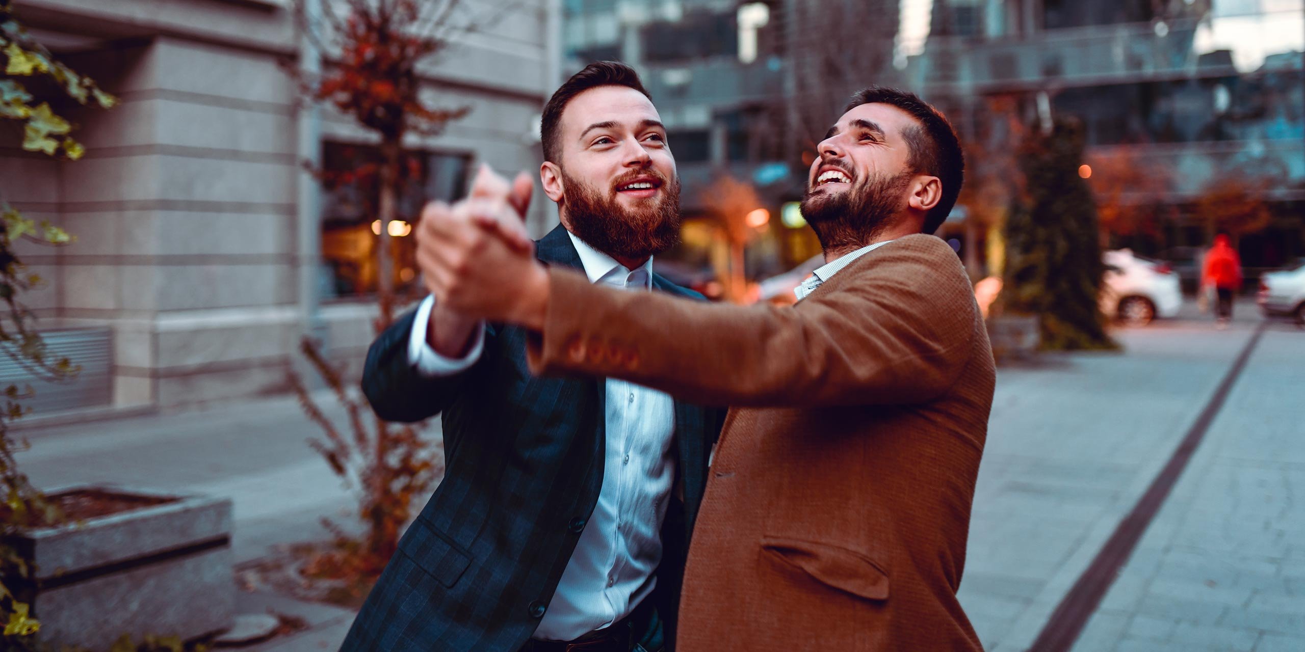 Zwei lachende junge Männer in Tanzhaltung vor einem Gebäude